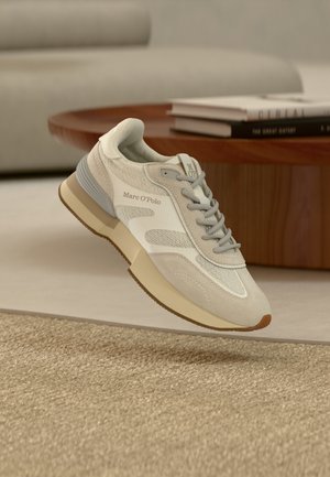 Jasnoszary sneaker wykonany z siateczki i zamszu, z gumową podeszwą i subtelnym logo. Posiada wyściełany kołnierz i teksturowane akcenty.