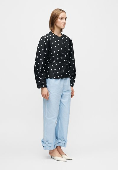 Juoda palaidinė su baltais taškeliais, apvali iškirptė ir pūsti rankovės. Šviesiai mėlynos kelnės su gėlių aplikacijomis apačioje. Balti smailūs bateliai.