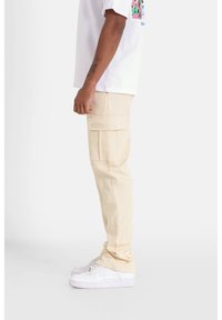 Beige cargobroek met meerdere zakken, rechte pasvorm, gemaakt van een katoenmix, gecombineerd met witte sneakers en een T-shirt met korte mouwen en een grafische print.
