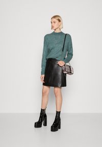 Tyrkysový pletený svetr, černá kožená mini sukně a černé lakované platformové kotníkové boty. Doplňující malá crossbody taška s vzorem.