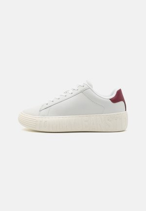 Sneaker med lav profil i hvid med tyk sål præget med "TOMMY JEANS" og rød hæl-plamage, vist i venstre side.