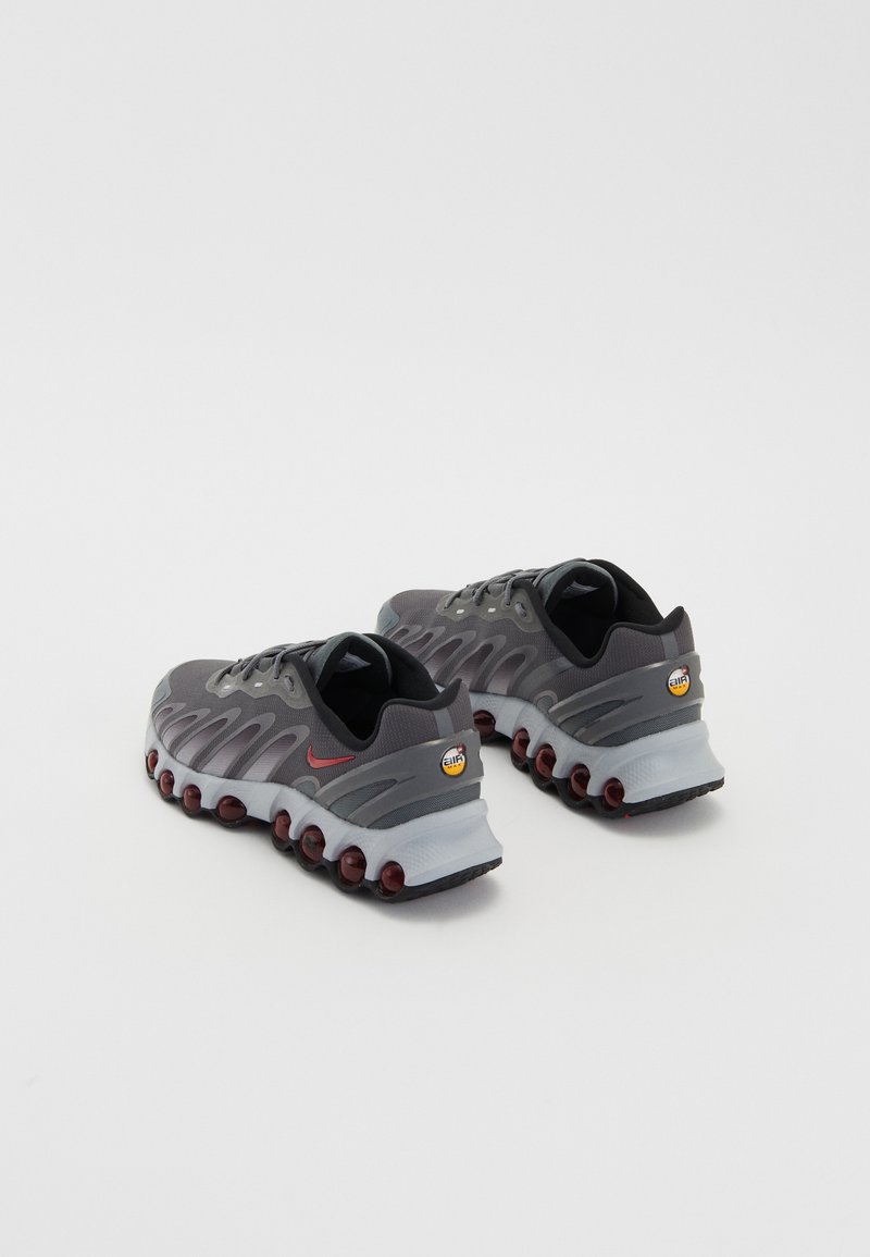 Zapatillas deportivas grises con un diseño elegante, que cuentan con un acento rojo, parte superior texturizada y cápsulas de amortiguación visibles en la suela.