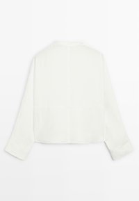 Vit långärmad skjorta med en kortad design, som har en mandarin-krage och diskreta sömnadsdetaljer längs ryggen och ärmarna.