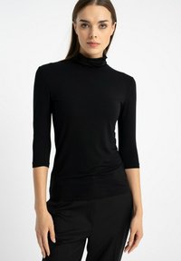 Czarna, długosleeve'owa bluzka z golfem, wykonana z miękkiego materiału, dopasowany fason z rękawami o długości trzy czwarte i gładką fakturą. Brak widocznych wzorów lub akcentów.