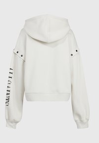 Vit kortärmad huvtröja med stor huva, börsiga axlar, svarta tryckknappar och "ALL CLAIMED" tryckt i svart på vänster ärm.