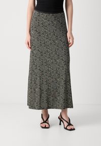 Falda maxi con un patrón en negro y beige, hecha de una tela ligera. Presenta una cintura ajustada y está combinada con sandalias de tacón negras.