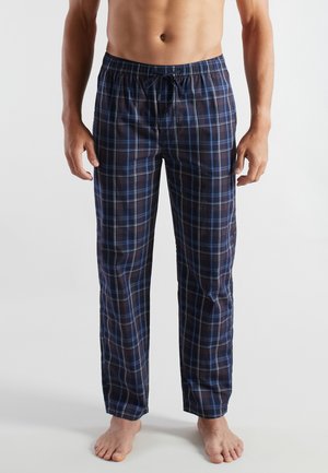 Oben ohne stehende Person, die marineblaue und schwarze karierte Schlafanzughose mit elastischem Bund und Kordelzug trägt, barfuß auf einem weißen Boden.