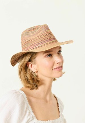 Woman with short blond hair wearing striped woven hat and white blouse, looking slightly upward and smiling gently.