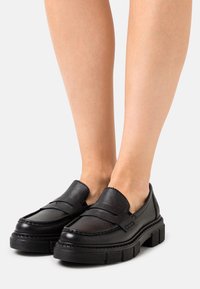 Mocassini in pelle nera con punta tonda e suola in gomma spessa. Presentano un design cucito e un dettaglio a strappo frontale. Rifinitura opaca.