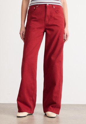 Person wearing high-waisted, wide-leg red pants with front pockets and button closure, paired with a striped top and cream shoes.