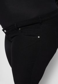Jeans de ganga pretos com um design ajustado, apresentando uma cintura de altura média, botões de metal prateado e bolsos frontais para funcionalidade.