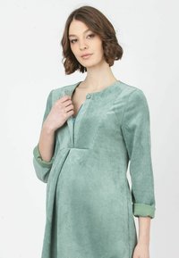 Vestido de pana verde menta con mangas tres cuartos, escote en V y cierre de botones. Presenta una superficie texturizada y bolsillos laterales.