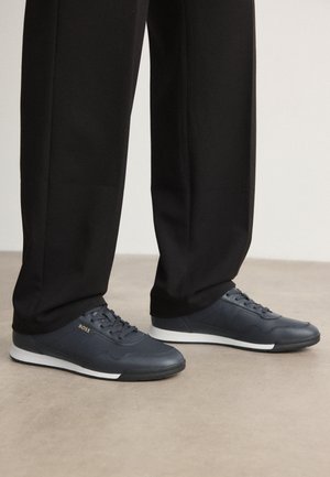 Navy blue sneakers made of leather with a textured finish, featuring white rubber soles and laces, branded with "BOSS" on the side.