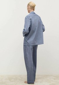 Komplet iz svetlo modrega denima, ki vključuje srajco in hlače. Sproščen kroj z dolgimi rokavi, ovratnikom in hlačami ravnega kroja. Mehka tekstura in minimalističen dizajn.