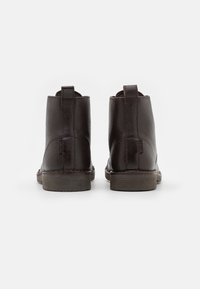 Botas de tobillo de cuero marrón con un acabado texturizado, punta redonda y tiradores en la parte posterior. Suelas de goma resistentes con un ligero tacón.