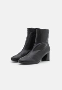 Une paire de bottines en cuir noir avec un bout rond et un talon bloc sur fond blanc.