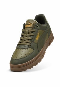 Baskets vert olive avec une tige en cuir, boîte à orteils perforée et semelle en caoutchouc marron. Dotées d'une fermeture à lacets et du logo Puma en orange.