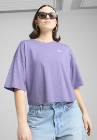 T-shirt cropped di colore lavanda con maniche corte e logo Puma bianco. Abbinato a pantaloni shorts in denim chiaro a vita alta.