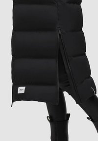 Abrigo acolchado negro con un diseño de quilt, cremallera lateral y parche con logo. El material es suave con un acabado mate.