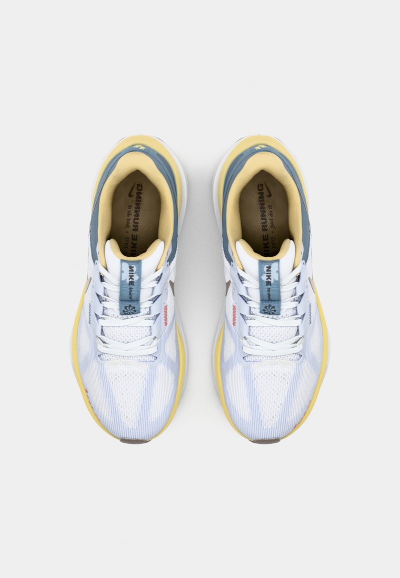 Zapatillas deportivas blancas con suelas amarillas, parte superior de malla, acentos azules y marca Nike en la lengüeta y el costado. Presentan cordones planos y un collar acolchado.