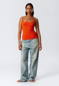Top a righe arancione infilato con spalline sottili abbinato a jeans a gamba larga blu chiaro. Bracciali e anelli argentati completano il look.