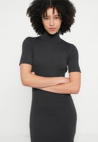 Ribbineulottu mekko, tummanharmaa, jossa korkea kaulus ja lyhyet hihat. Tiimalasimaista siluettia korostava vartalonmyötäinen malli ja sileä pinta.