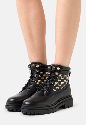 Bottines en cuir noir avec motif doré du logo MK, bout rond, col rembourré et semelle en caoutchouc épaisse avec traction. Accents en matériel doré.