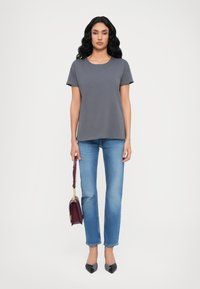 T-shirt gris à manches courtes associé à un jean droit bleu clair. Le modèle tient un sac à main bordeaux et porte des escarpins noirs à bouts pointus.