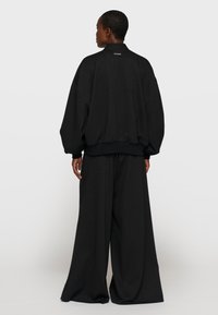 Chaqueta negra grande con textura, cuello redondeado, puños acanalados y pantalones anchos a juego. Sutil patrón de rayas finas en toda la prenda.