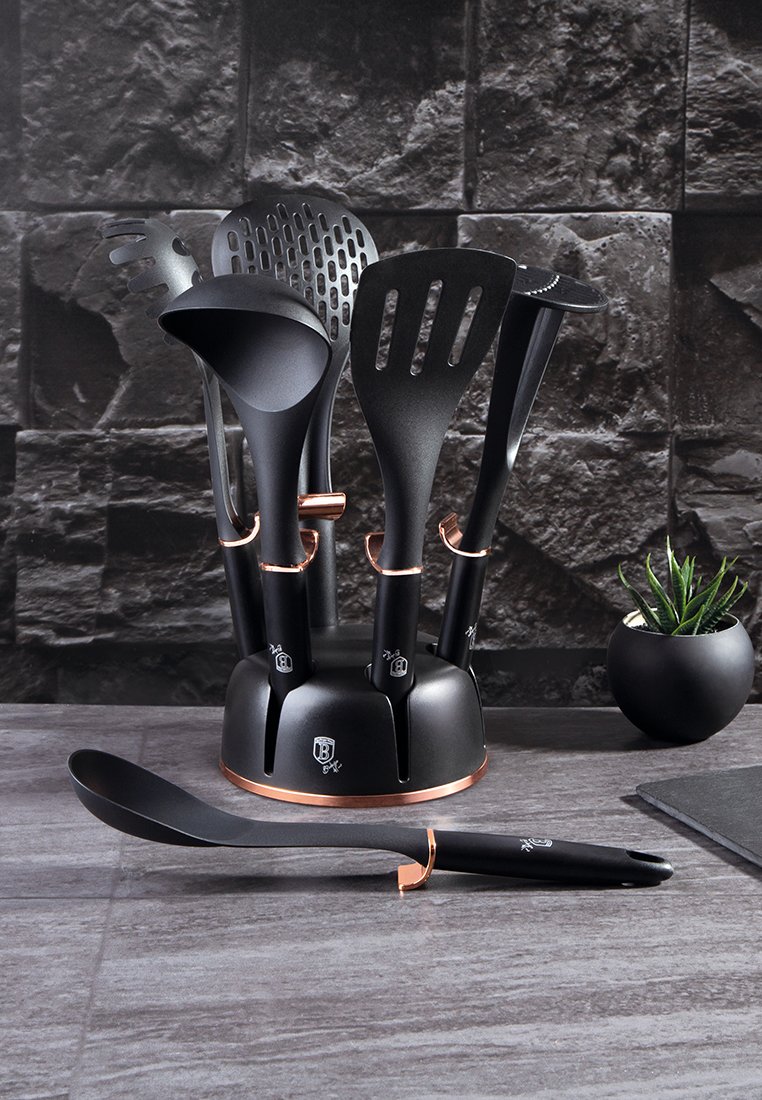 Černá sada kuchyňských nástrojů s držákem, zahrnující obracečku, hubičku, naběračku a stěrku. Akcenty v mědi. Hladký plastový povrch.