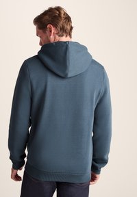Hooded sweatshirt in dark teal, featuring a soft, textured fabric, ribbed cuffs, and a relaxed fit. Back view shows the hood and seam details.