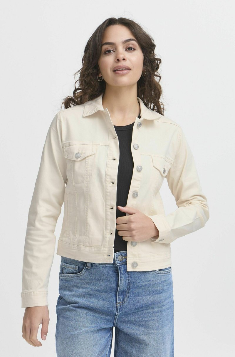 Veste en jean beige clair avec un col, fermeture à boutons sur le devant, deux poches poitrine et manches longues, associée à un jean bleu.