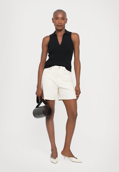 Black ribbed sleeveless top with a collar, white shorts, and a small black circular bag. White heeled shoes with a pointed design.