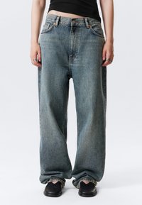 Φθαρμένο μπλε τζιν με φαρδιά γραμμή, σχέδιο με πέντε τσέπες, ενισχυμένες ραφές και εμφανείς λεπτομέρειες εξαρτημάτων. Διακοσμημένο με ευθεία γραμμή στο πόδι.