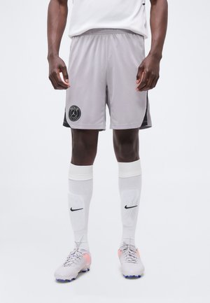 Szürke, párizsi logós sport rövidnadrágot, fehér térdig érő Nike zoknit és stoplis cipőt viselő férfi áll egy egyszínű háttér előtt.