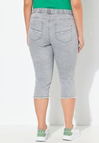 Pantalones capri de mezclilla gris con dobladillo deshilachado, cintura elástica y dos bolsillos traseros. Llevados con zapatillas blancas con acentos verdes.