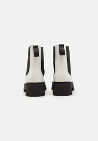 Botine negre și albe cu talpă groasă, panouri laterale elastice și o etichetă cu marcă în spate. Talpă din cauciuc texturat.