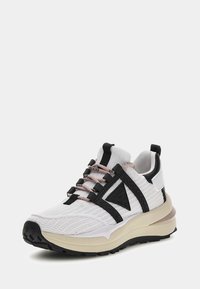 Sneaker bianco con tomaia in rete, dettagli neri e lacci rosa pallido. Suola intermedia beige spessa e suola esterna nera texturizzata. Logo sul lato.