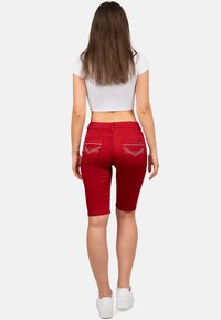 Bermuda shorts in denim rosso con un design aderente. Presentano tasche posteriori con cuciture a contrasto. Abbinati a sneaker bianche.
