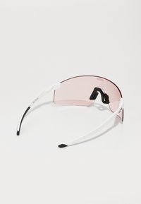Lunettes de soleil avec un grand verre rose, une monture blanche et des embouts de branches noirs. Elles présentent un design minimaliste sans quincaillerie ni embellissements visibles.