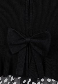 Tissu tricoté côtelé noir avec un grand nœud noué au centre au-dessus d'une jupe plissée à motifs abstraits noirs et blancs.