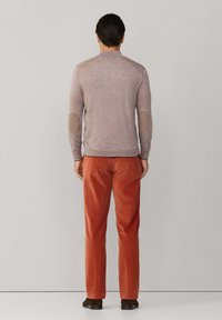 Grijze gebreide trui met elleboogpatches, gecombineerd met oranje corduroy broek. De trui heeft een hoge halslijn en een getailleerd ontwerp.