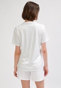 Biała sportowa koszulka z krótkim rękawem, gładka tkanina, okrągły dekolt, luźny krój, zestawiona z białymi szortami, minimalistyczny design, brak widocznych wzorów.