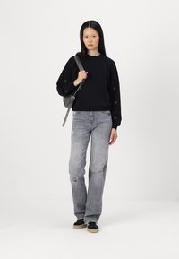 Czarny sweatshirt z haftem serca na rękawach, połączony z jasnoszarymi, zniszczonymi dżinsami i czarnymi sneakersami z beżową podeszwą.