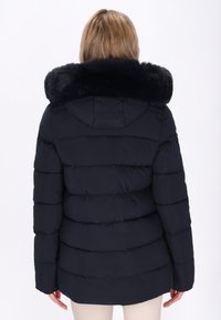 Dunkelblaue Steppjacke mit einem Kunstfellkragen, ausgestattet mit horizontalen Steppnähten, einer Kapuze und langen Ärmeln. Glatte Textur und warmes Design.