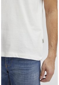 Hvid bomulds T-shirt med korte ærmer, en afslappet pasform, buet kant og diskret sideetiket. Bæres med blå denim jeans.
