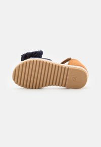 Lapsen sandaalit, joissa on uritettu kumipohja, tummansinisestä kankaasta valmistettu nilkkaremmi ja vaaleanruskea mokkanahkapeite varpaiden kohdalla. Koko 26 näkyy pohjassa.