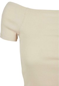 Beige ribbad off-shoulder topp med korta ärmar. Tyget har en mjuk textur och en subtil stretch, vilket visar en figurnära design.