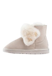 Botte en daim beige avec un doux revers en fourrure crème et deux boutons en bois en forme de flocon de neige décoratifs. Semelle plate avec des détails de couture.
