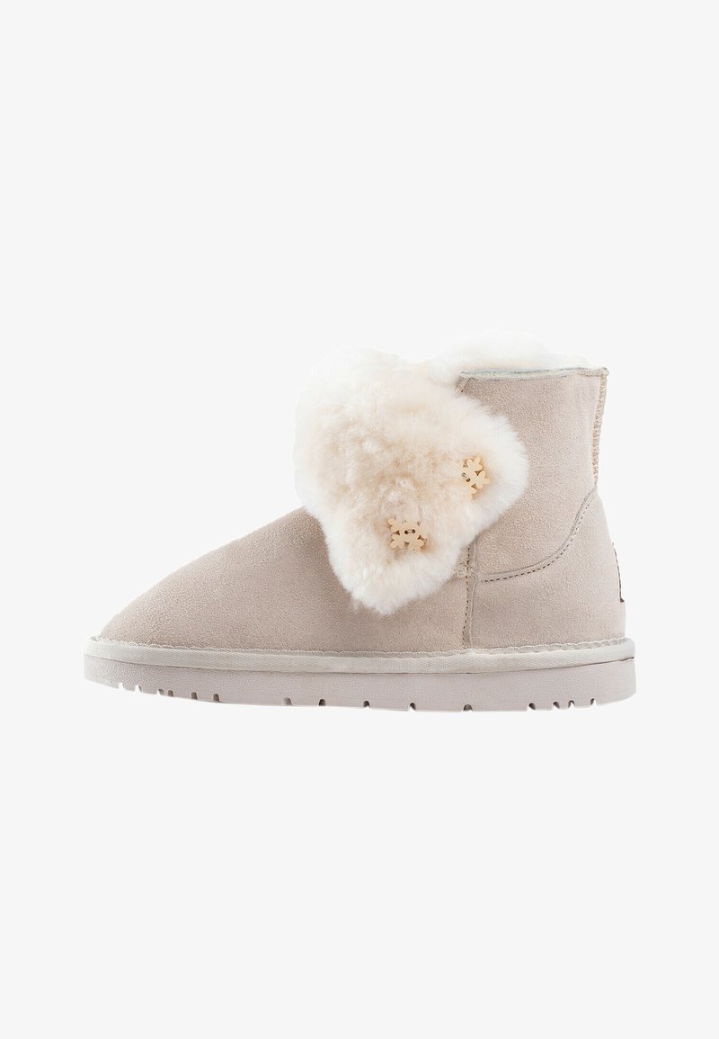 Boots in camoscio beige con un morbido risvolto in pelliccia crema e due pulsanti decorativi a forma di fiocco di neve in legno. Suola piatta con dettagli di cucitura.